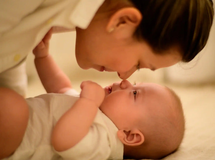 Baby lying on its back while an adult leans over, their noses touching gently.