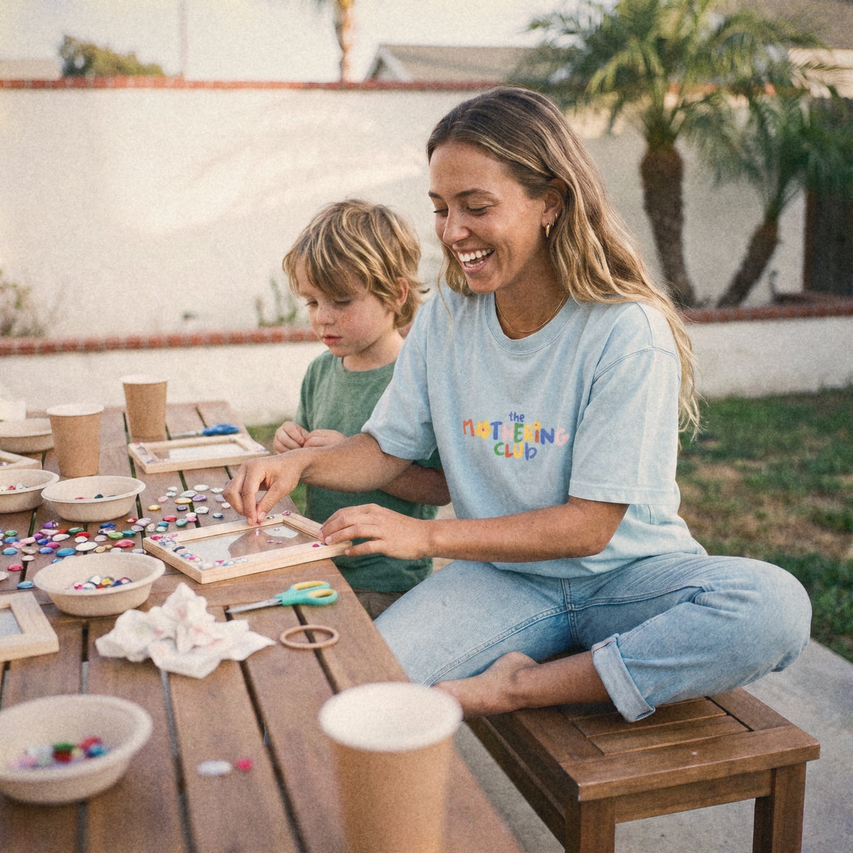 Mom in the Mothering Club Logo Tee at a craft table with her son