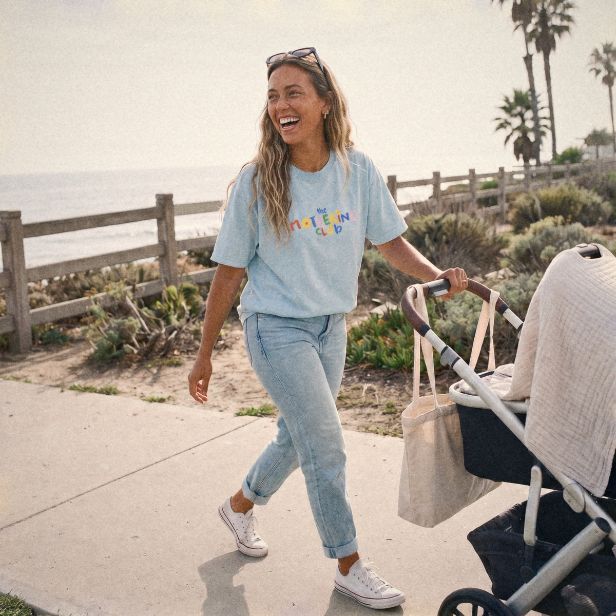Mom in the Mothering Club Logo Tee walking a stroller by the beach