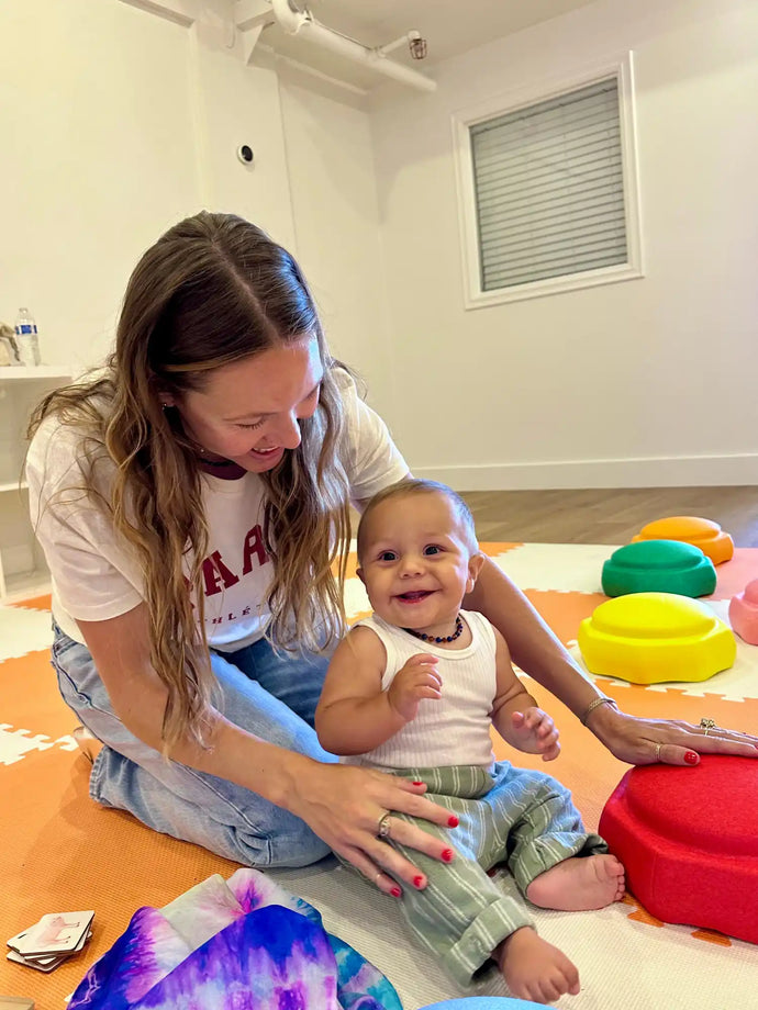 Two people sitting on a colorful play mat with toys.
