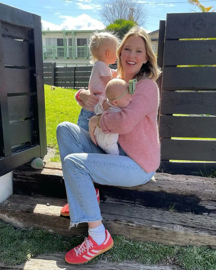 Woman holding two young children while sitting on a wooden structure outdoors.